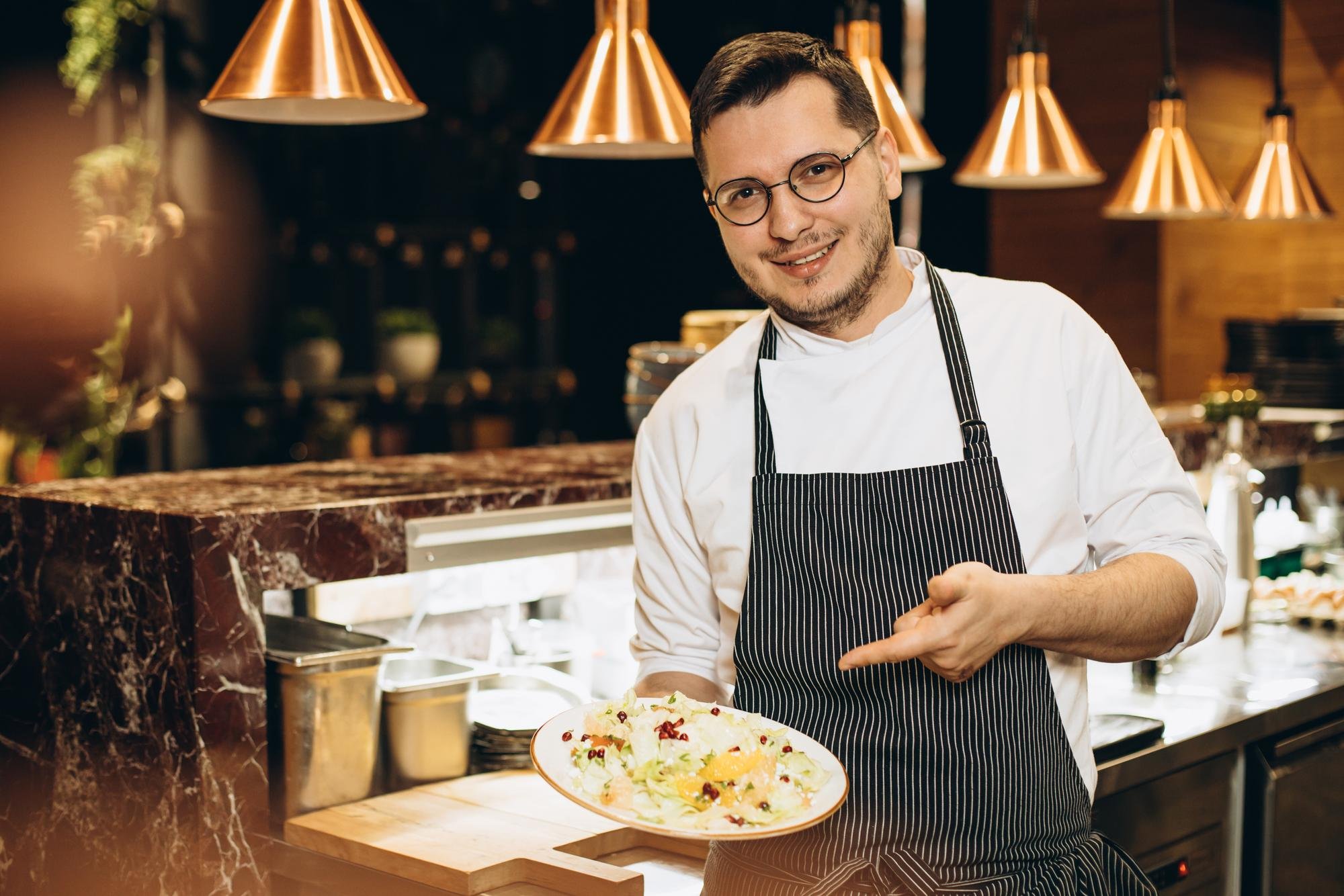 Chef in a professional kitchen holding a plated dish